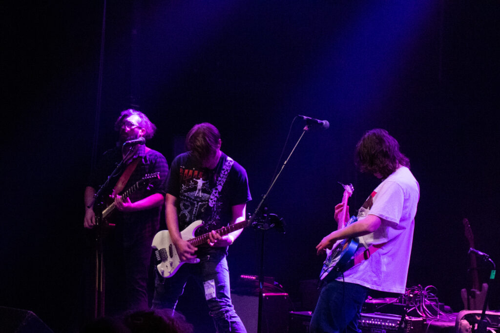 A band playing a song, lit with purple lights