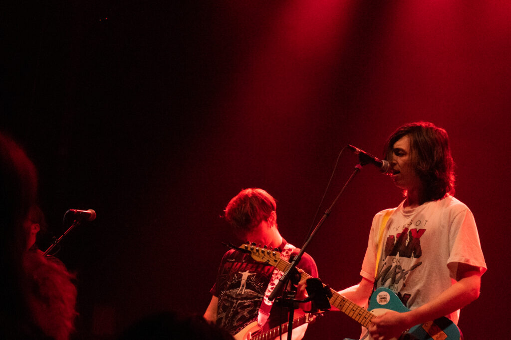 A photo of a lead singer with long hair in his face, and a guitarist, bathed in red light